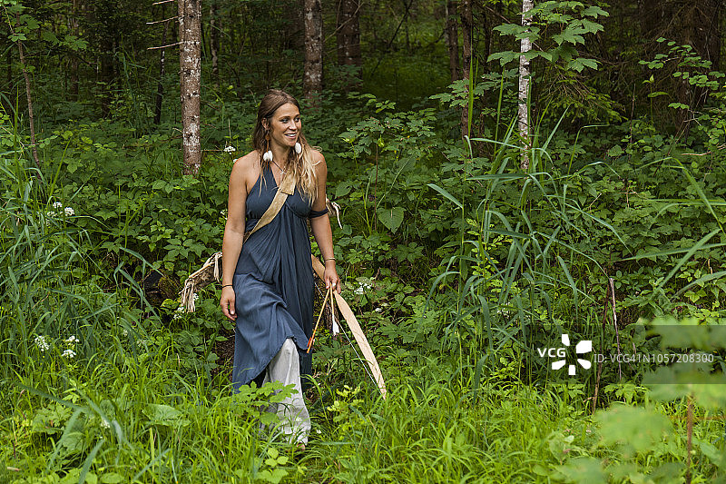 微笑的女人在森林里带着弓箭行走图片素材