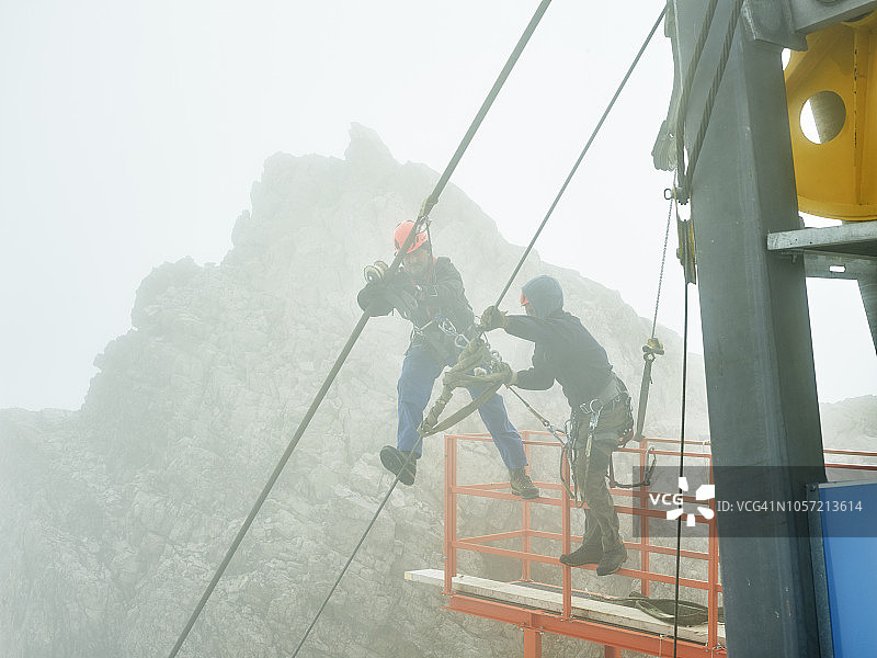 德国巴伐利亚加米施-帕滕基兴楚格峰：安装工人在货物缆车钢索上工作图片素材