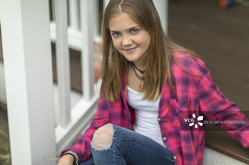 坐在门廊台阶上微笑的年轻女孩的肖像图片素材