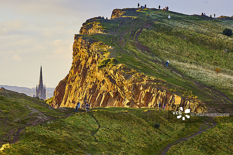 阳光照耀下的索尔兹伯里峭壁岩石，爱丁堡荷里路德公园的教堂尖顶图片素材