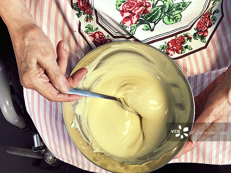 残疾老妇人在碗里搅拌融化的白巧克力图片素材