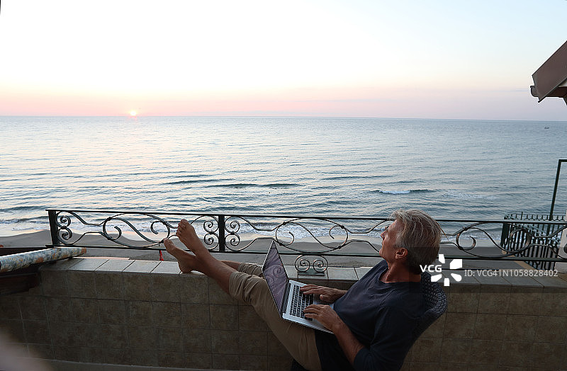 男子在笔记本电脑上工作，眺望大海图片素材