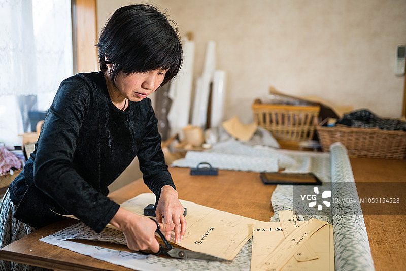 年长妇女裁剪织物在她的小型纺织商店。图片素材