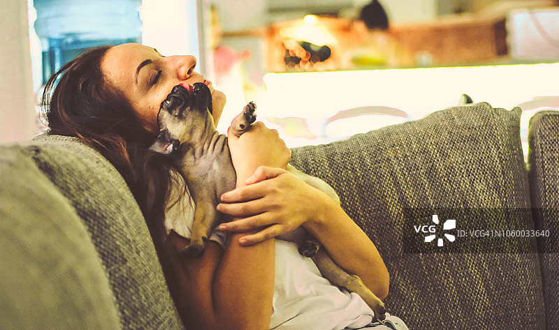 在客厅里和巴哥犬坐在一起的年轻女人图片素材