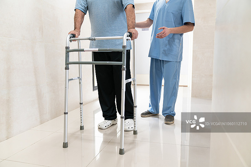 老年人使用助行器，护士在他身后的特写图片素材