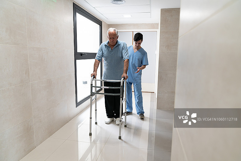 男护士帮助老年病人使用助行器行走图片素材