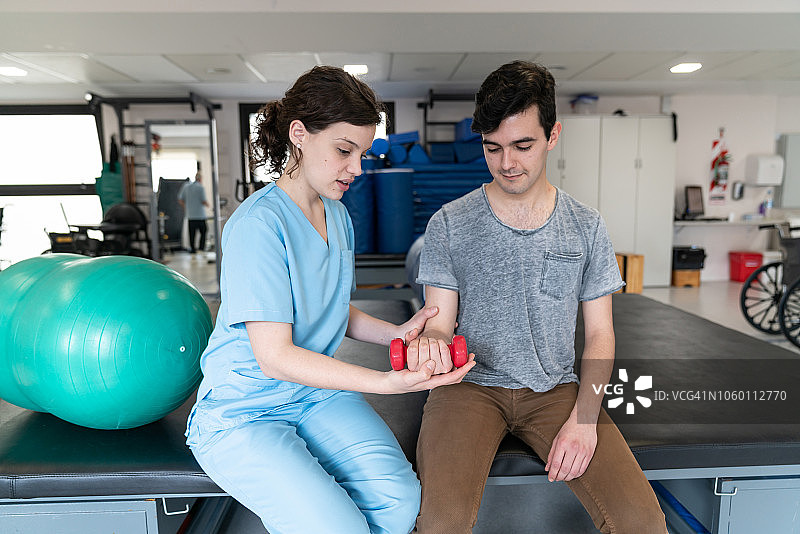 年轻的理疗师帮助男病人进行手臂负重训练图片素材