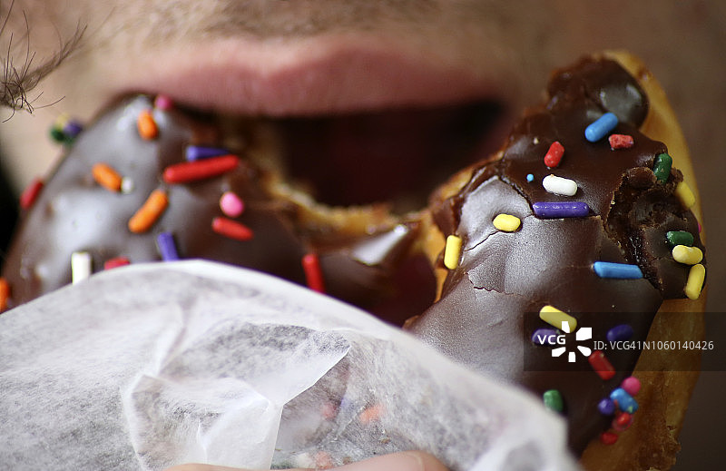 咬着巧克力甜甜圈的嘴部特写，带有糖屑图片素材