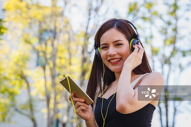 快乐的年轻女子在公园户外戴耳机听音乐图片素材