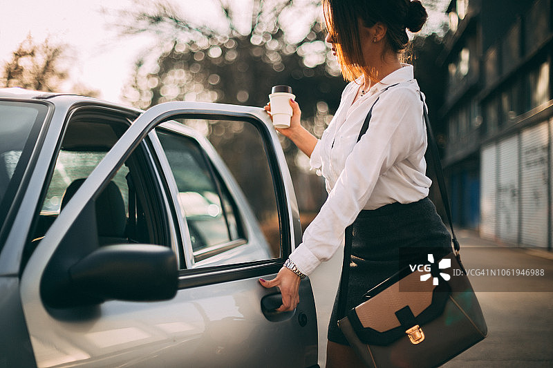 早上买咖啡后进入汽车的商务女性图片素材
