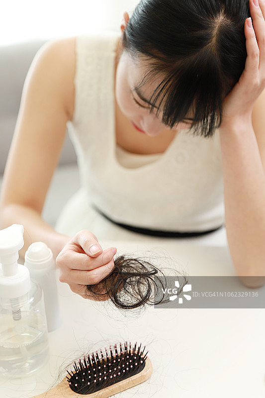 女人拿着掉落的头发，表情担忧图片素材