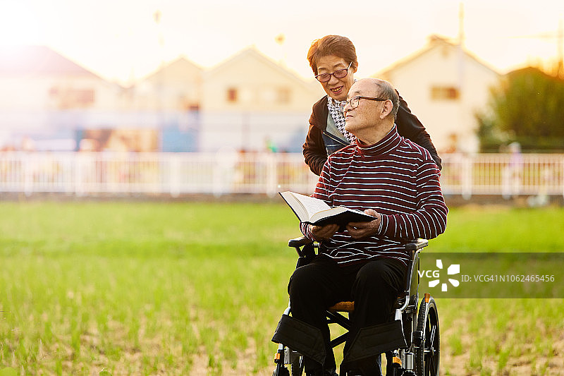 微笑的妻子在辅助生活中心照顾坐轮椅的人，男人手拿一本书图片素材