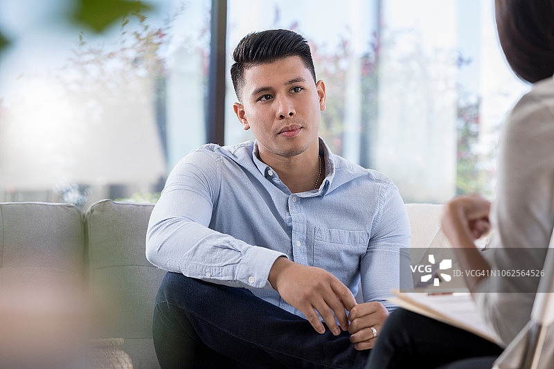 年轻男人在沙发上专注地听咨询师讲话图片素材