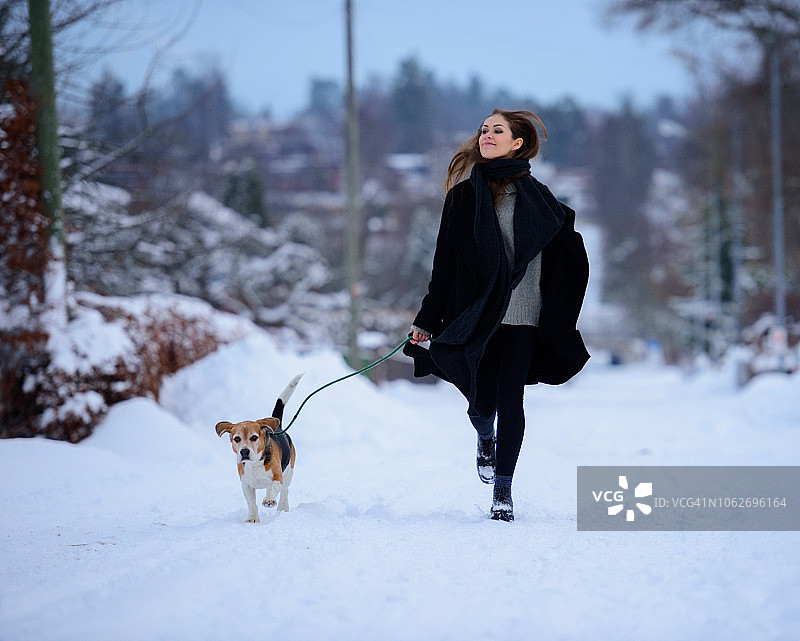 快乐的女人在冬日街道上和比格犬一起跑步图片素材