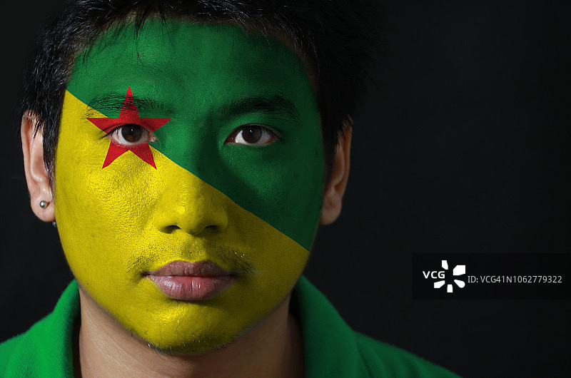 黑色背景下，脸上画着法属圭亚那国旗的男子肖像图片素材