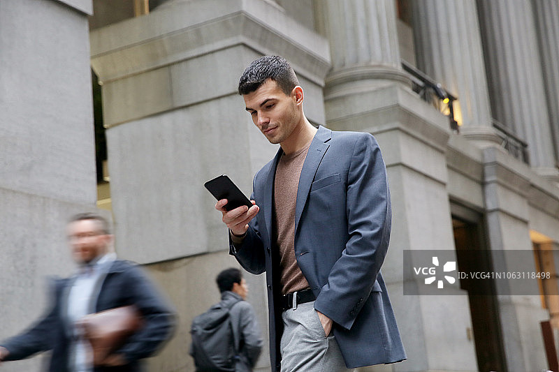 纽约金融区内查看手机的年轻千禧一代商务男士仰视图片素材