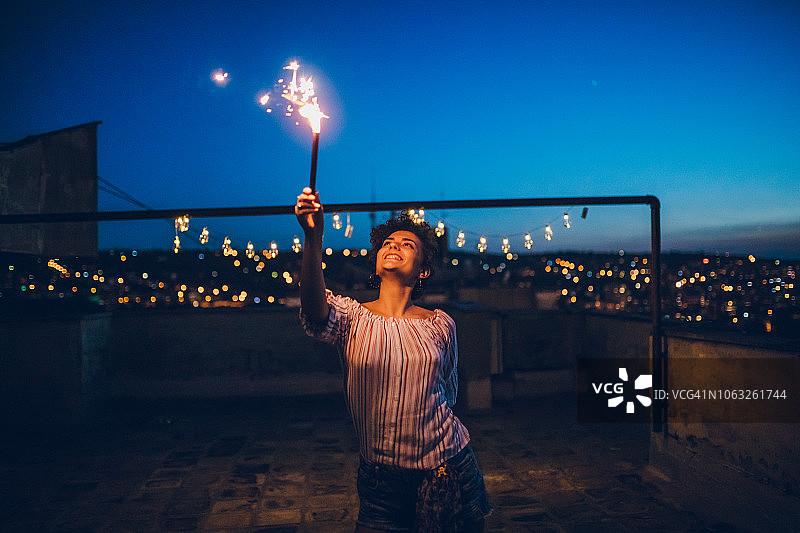 在屋顶上手持烟花的年轻女人图片素材