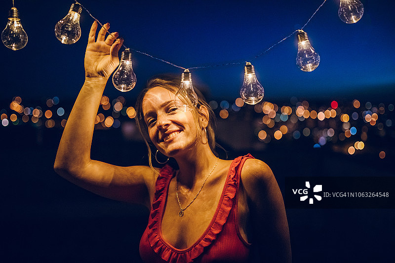 在屋顶上手持串灯的年轻女人图片素材