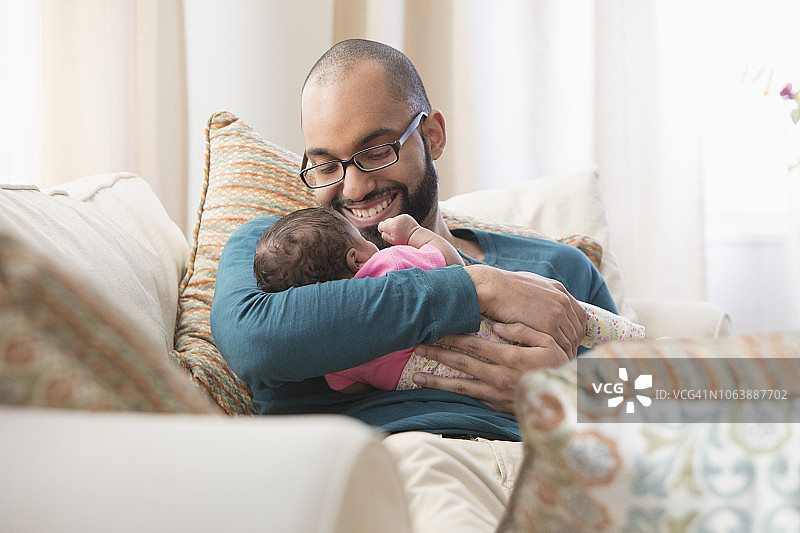 年轻的拉丁裔父亲抱着他的新生婴儿坐在沙发上图片素材