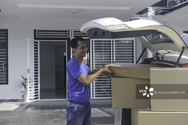 亚洲男人从汽车后备箱卸货搬进新家图片素材