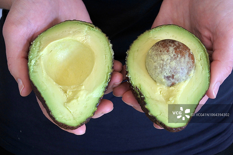 手持切开的鳄梨果实两半的女人图片素材