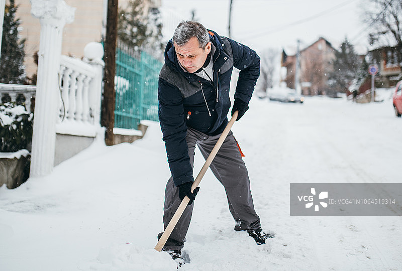 用雪铲清理人行道的年长男人图片素材