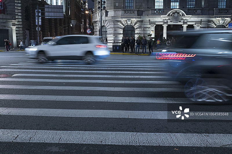 夜间人行横道上快速行驶的汽车，背景建筑为上海外滩图片素材
