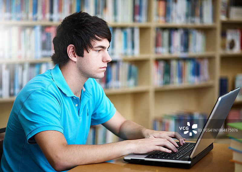 在图书馆用笔记本电脑工作的男学生图片素材