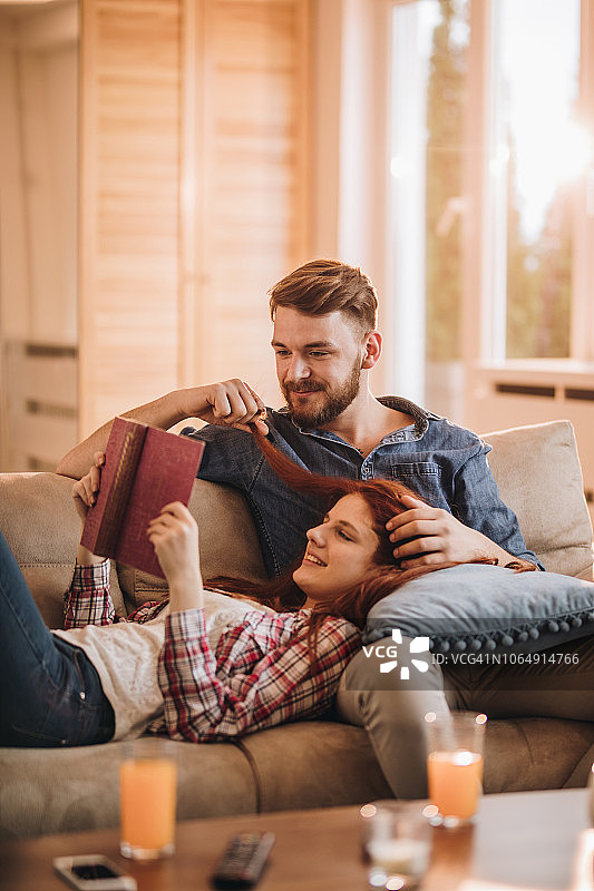 年轻情侣在客厅沙发上阅读书籍图片素材