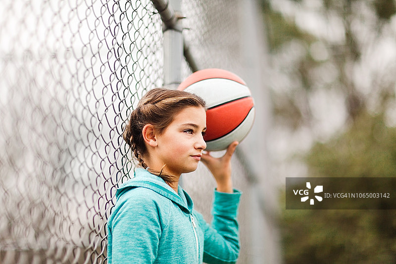 在操场倚着链条围栏，抱着篮球的少女图片素材