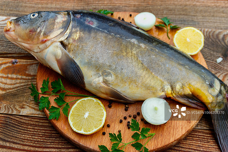 生鲤鱼配柠檬洋葱欧芹，砧板上，木桌旁图片素材