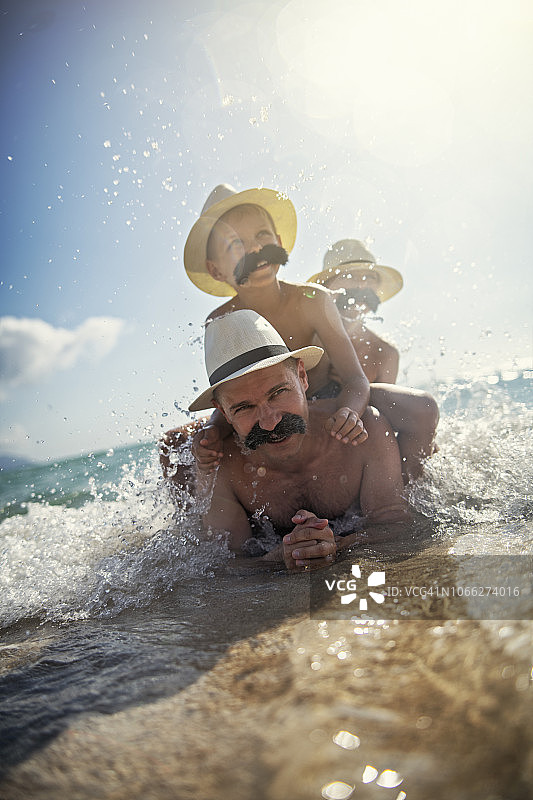 有趣的父亲和儿子们在海边玩耍，留着小胡子图片素材