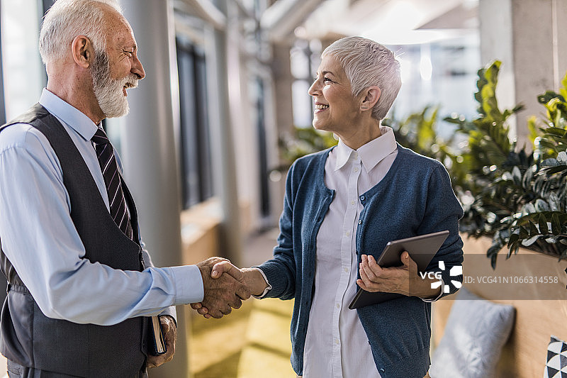 快乐的年长商业伙伴在走廊里互相问候。图片素材
