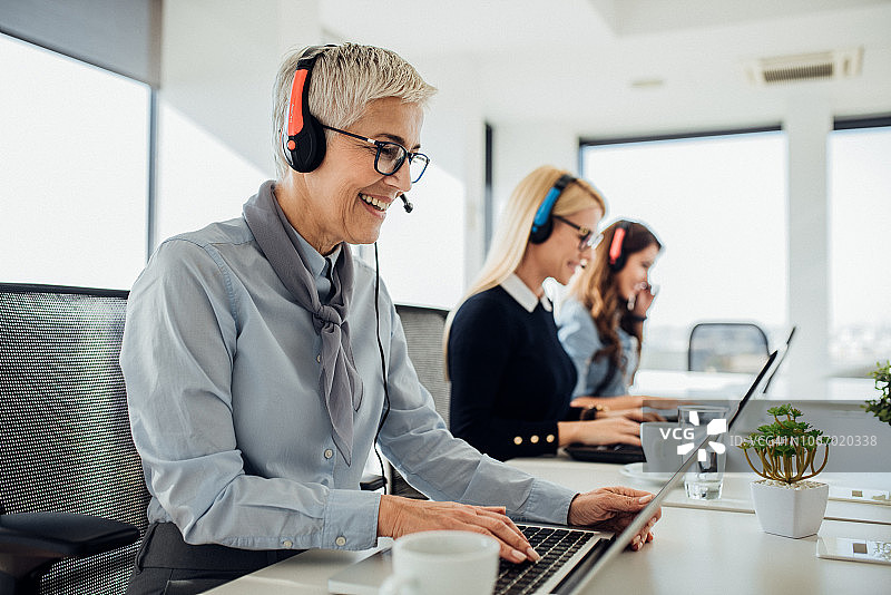 使用笔记本电脑的微笑的呼叫中心工作人员图片素材