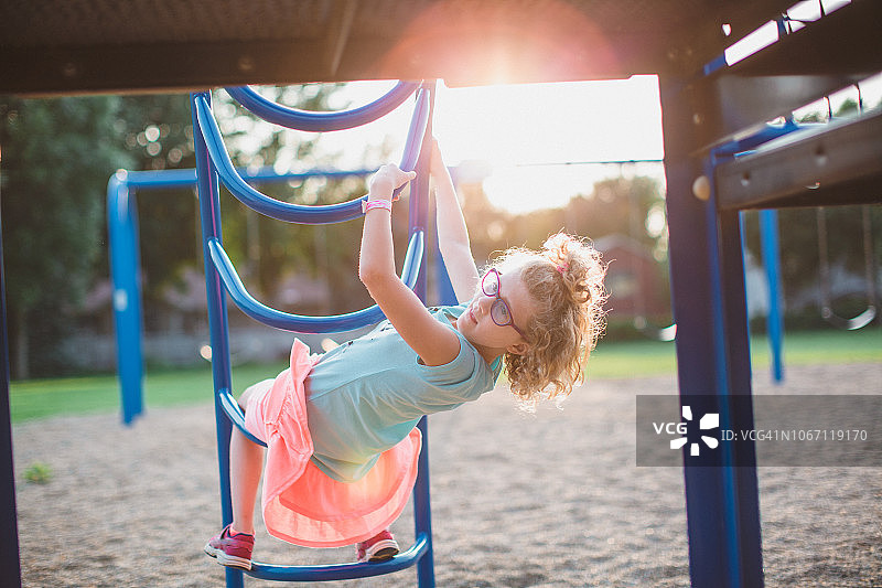 女孩悬挂在儿童乐园的攀爬架上图片素材