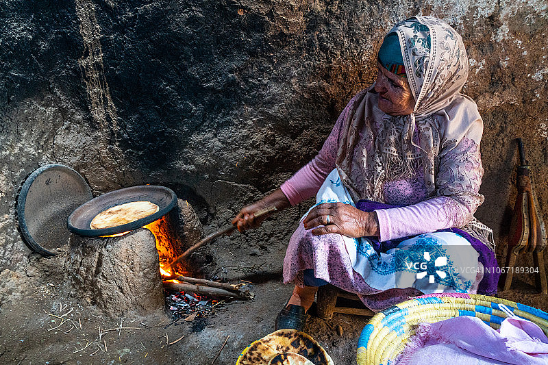 身着传统服装的柏柏尔老妇人在明火上观看塔吉锅午餐的肖像，摩洛哥阿古恩桑，高阿特拉斯图片素材