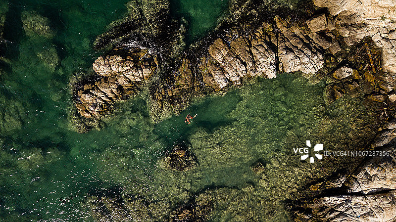 男人在岩石礁石旁的海里游泳图片素材