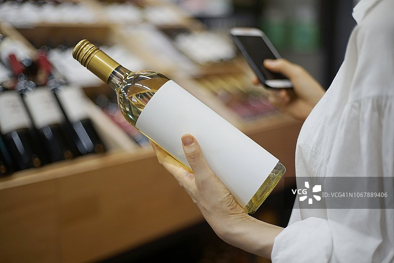 女人在酒类商店用手机选择葡萄酒图片素材