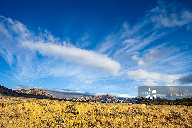 金色草原的广阔景象，深蓝色天空和花岗岩山脉映衬着戏剧性的云彩。图片素材