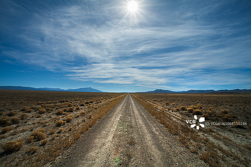 穿过广阔平坦沙漠景观的空旷砂石单车道土路的主观视角，天空中有太阳图片素材