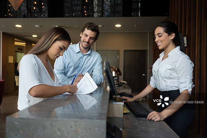 漂亮的女人在酒店办理入住手续，与伴侣和友好的接待员一起微笑工作图片素材
