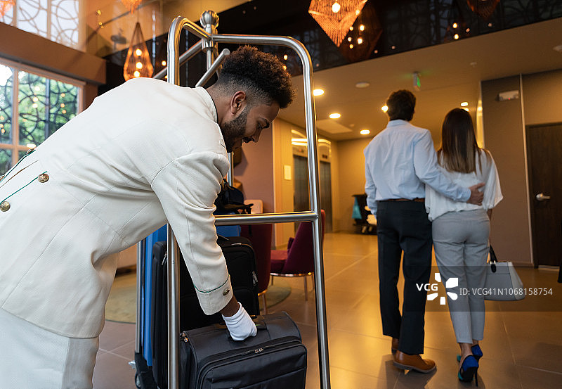 酒店的黑人行李员将客人的手提箱放在行李车上图片素材