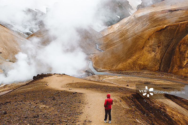 在冰岛凯灵加峡湾地热山区行走的红衣男子图片素材