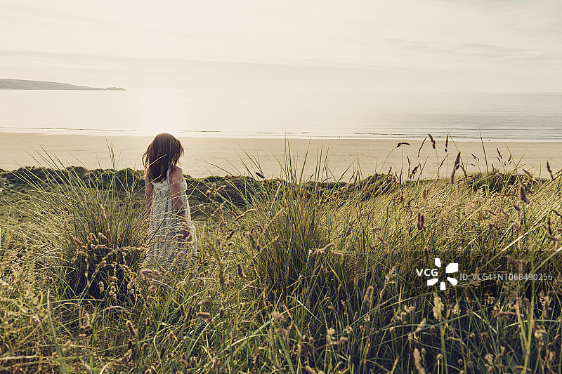 穿着飘逸长裙走在沙丘上，走向康沃尔郡格维西安托万斯海滩日落的女人图片素材