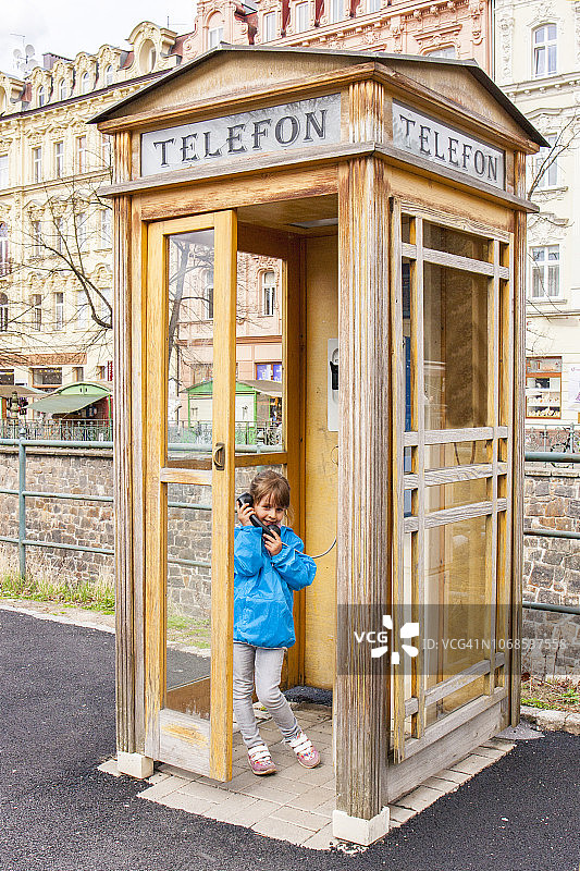 在捷克卡罗维发利温泉度假中心用公用电话交谈的小女孩图片素材