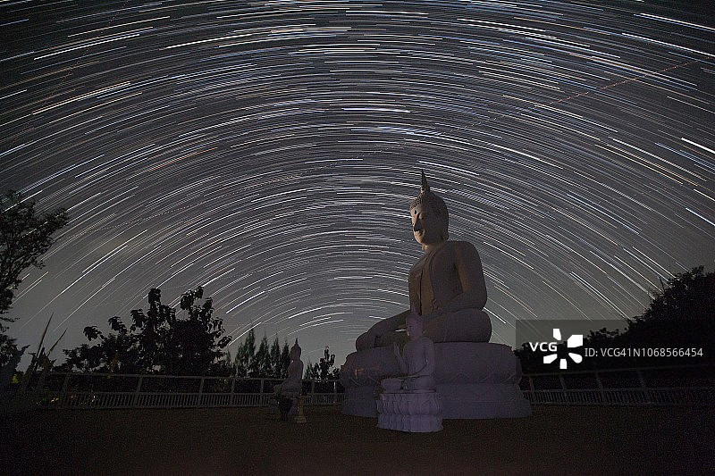 白色大理石佛像在户外冥想，夜间有美丽的星轨图片素材