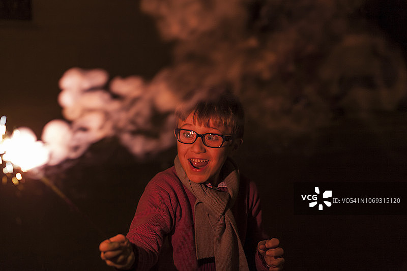 在夜晚，孩子手持烟花，面露喜色（西班牙）图片素材