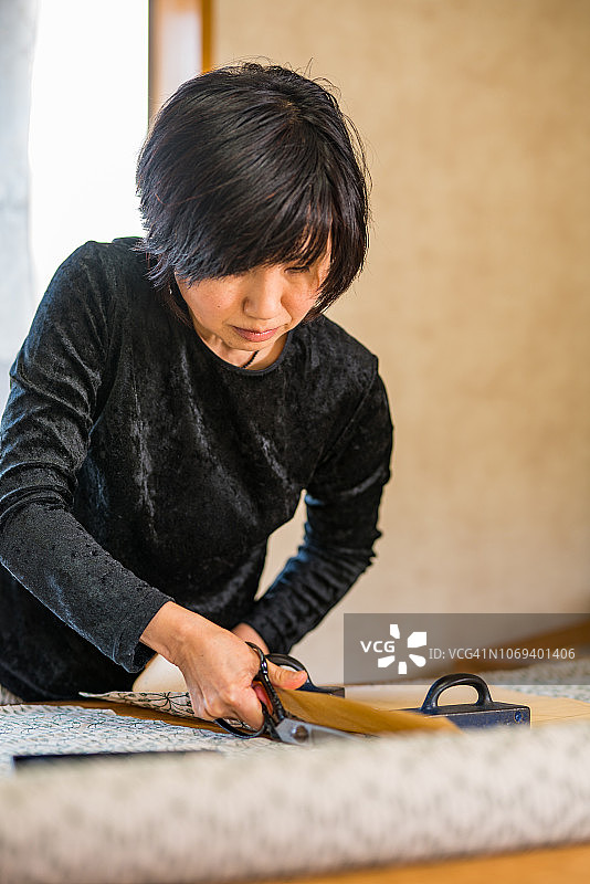 年长妇女裁剪织物在她的小型纺织商店。图片素材