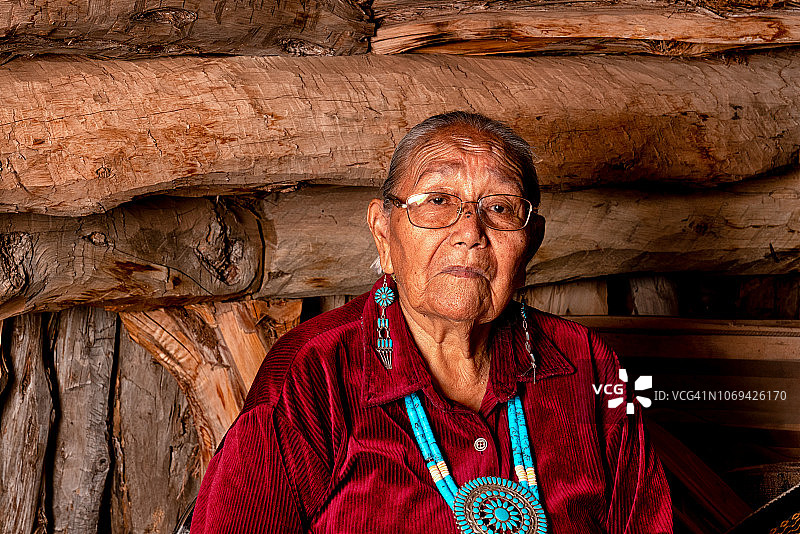 在传统霍根屋内摆姿势的美丽的85岁纳瓦霍族美国原住民老妇人图片素材