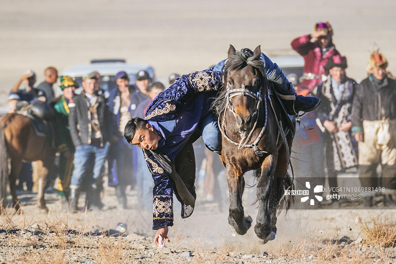 库米斯阿卢（或廷格伊卢）活动，字面意思是“捡硬币”。这个游戏是对骑术的考验，因为它要求参赛者全速飞奔，同时伸手捡起地上用布包裹的硬币。图片素材